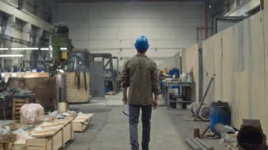 Her gün yapılan teftiş sırasında, sert şapkalı bir erkek yöneticinin metal fabrikası boyunca yürüdüğü arka plan görüntüsü.