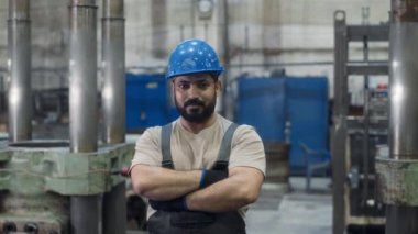 Orta Doğulu erkek torna işçisinin orta boy portresi. Mavi şapkalı fabrika işçisi. Kameraya katlanmış elleriyle poz veriyor.