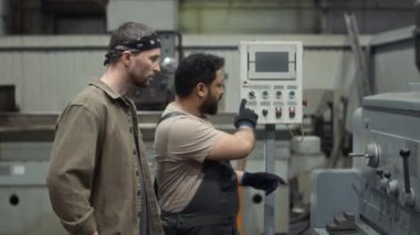 CNC değirmen makinesinin yeni çalışanlarına nasıl çalıştırılacağını gösteren Orta Doğulu erkek metal fabrikası işçilerinin görüntüsü.