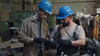 Çok ırklı iki erkek mühendisin, fabrikada makine ekipmanlarını tamir ederken ya da monte ederken orta boy çekimleri.