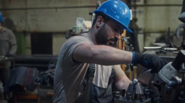 Orta Doğulu erkek teknisyen, tulumlu ve mavi kasklı metal fabrikasında makineleri tamir ediyor.