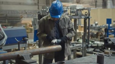 Erkek endüstriyel işçinin güvenlik gözlüğü ve kasket taktığı el değirmeni makinesiyle fabrikada metal üzerinde çalıştığı orta boy bir fotoğraf.