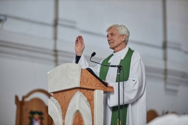 Sunağın arkasında duran ve kilisedeki insanları kutsayan kıdemli rahip.