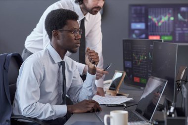 Genç simsarlar, broker ofisindeki masada otururken bilgisayar monitörlerine bakan yüksek göstergeler bekliyorlar.