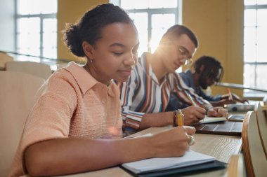 Üniversite öğrencileri, ders sırasında masa başında oturup not defterlerine yazıyorlar.