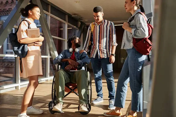 Student with disability sitting on wheelchair and talking to classmates while they standing in school corridor during break