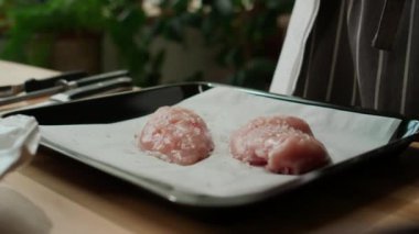 Parşömen kağıdında ızgaranın üzerinde duran iki çiğ tavuk göğsünü tuzlayan tanınmayan bir aşçı.