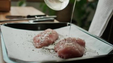 İki baharatlı tavuk göğsü filetosunun üzerine zeytinyağı döküp ızgara kağıdının üzerine serpiştirilmiş tanınmamış bir aşçı.