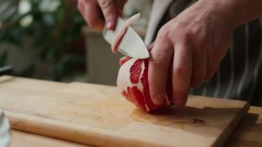 Ahşap yemek masasında greyfurt soyarken keskin bıçak kullanan tanınmayan bir erkek aşçının görüntüsü.