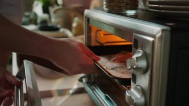 Tanınmayan erkek şefin, iki tavuk bifteğiyle birlikte elektrikli mini fırına koyduğu yavaş çekim.