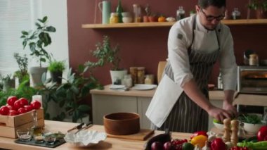 Beyaz erkek şefin, açık mutfakta öğle yemeği pişirirken taze yeşil salata yapraklarını kaseye atarken orta boy el resmi.