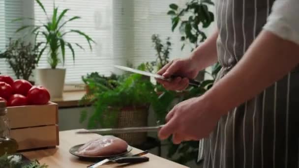 料理を始める前にキッチンでナイフを研ぎながら筋肉を使ったストライプエプロンで認識できない男性シェフのクロップショット — ストック動画