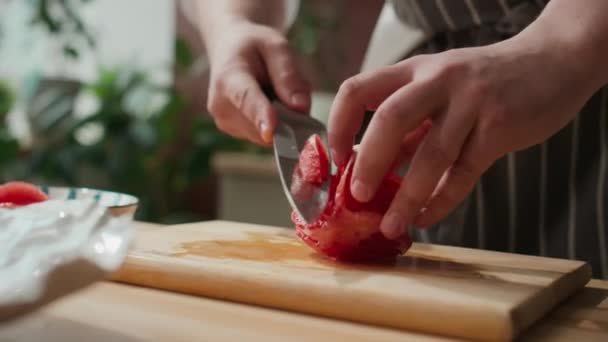 認識できないシェフの手のクロップショット キッチンの木の切断板にジューシーな赤いグレープフルーツをスライス — ストック動画