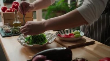 Beyaz seramik tabakta roka salatasına taze greyfurt dilimleri eklemek için paslanmaz çelik forseps kullanan tanınmayan bir erkek aşçı.