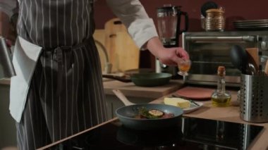 Çizgili önlüklü, tanınmayan bir erkek aşçının bifteği kızartılmış tavada ve otlarla pişirdiği kavurucu kullanması.