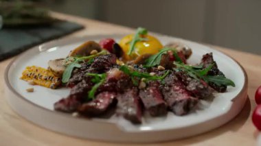 Pişmiş bifteğe yakın çekim ve mutfakta beyaz tabakta mikro yeşille dekore edilmiş kızarmış sebzeler.