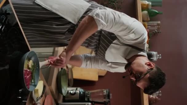 キッチンでフライパンに赤肉ステーキ タイム ニンニクを調理する白人男性シェフの垂直中型ショット — ストック動画