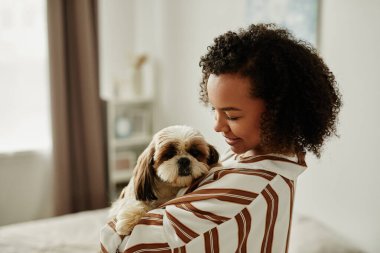 Evcil köpeğini kucağında tutan ve gülümseyen siyahi bir genç kadın portresi.