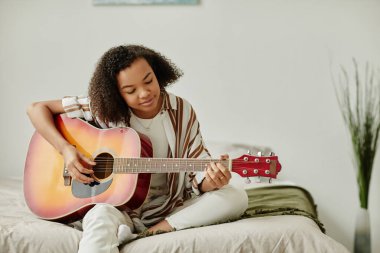 Evde akustik gitar çalan, hobilerinden zevk alan, fotokopi çeken siyahi genç bir kadının minimal portresi.