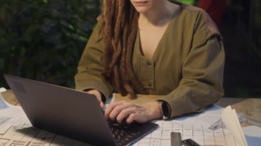 Beyaz kadın mühendisin, yeşil üretim fabrikasındaki saksı bitkilerinin arasında otururken dizüstü bilgisayara bakıp daktilo kullanırken belden yukarı çekilen görüntüsü.