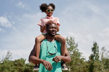 Mutlu genç baba kızını omuzlarına alıyor ve onunla temiz havada vakit geçiriyor.