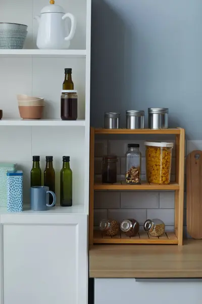Vertical image of kitchen cupboard with containers with cereals and oil standing on shelves