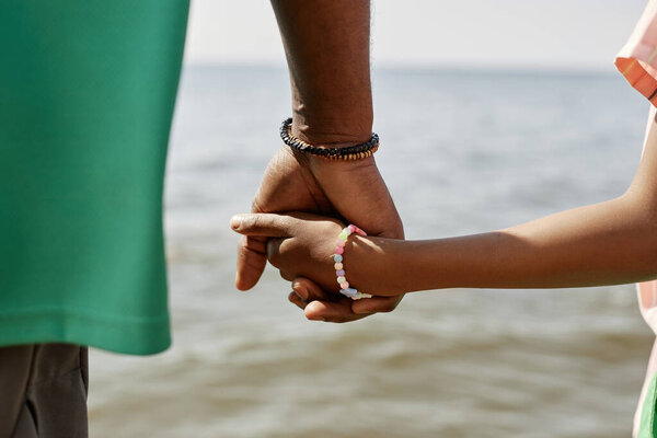 Close-up of dad holding hands with his little daughter during their walk on the beach