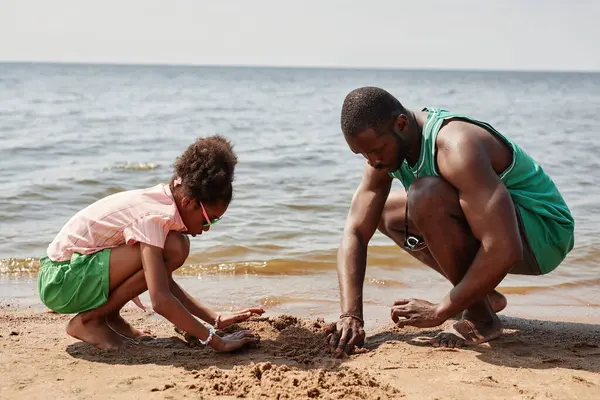 African American dad building sand castle together with his little daughter while they spending time on the beach