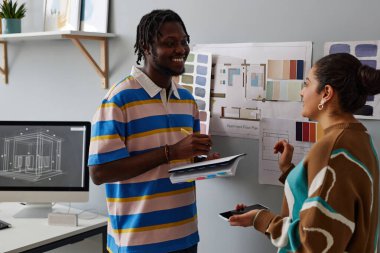 Ofisteki meslektaşıyla konuşurken not defterine notlar alan gülümseyen genç adam.