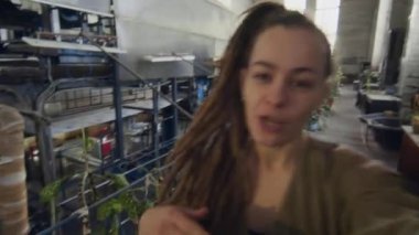 Haki rengi örtülü beyaz kadın fabrika işçisinin el bilgisayarı. Üretim fabrikasında yeşil bitkiler yetiştiriyor ve vlog kaydediyor.