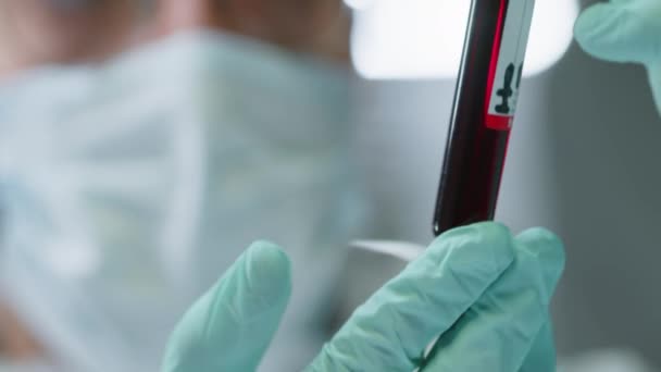 无法辨认的戴口罩的戴口罩的科学家在实验室研究时在9Ml试管中保持和检测红液的方法 — 图库视频影像