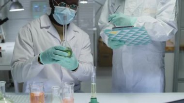 Laboratuvarda kimyasal deneyler yapan iki çok ırklı mikrobiyoloğu yukarı kaldır, masada cam sıvıları karıştır, tepkiyi izle ve not al.