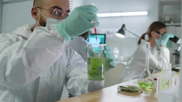 聚精会神的中东男性科学家在现代实验室的桌上做研究时 在玻璃杯烧杯中加入红色液体 — 图库视频影像