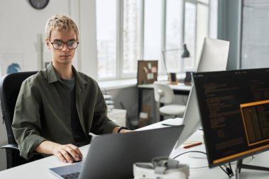 Gözlüklü genç programcı ofisinde otururken yeni yazılımın kodlarıyla işine konsantre oluyor.