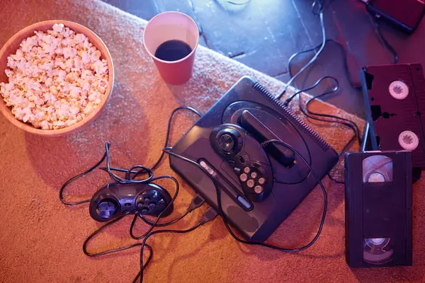 Top view at retro videogame console with popcorn and video tapes, copy space