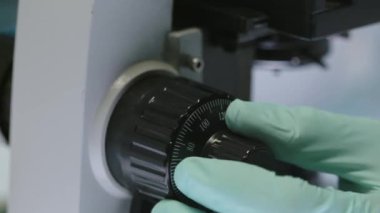 Laboratuvarda gözlemler yaparken mikroskoba odaklanan tanınamayan eldivenli bilim adamlarının yakınlaşması.