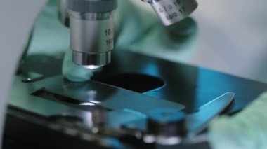 Laboratuvarda analiz yapmadan önce cam sürgüyü mikroskoba yerleştirip ekipmanları ayarlayan bilim adamının tanımlanamayan eldivenli ellerine yakın çekim