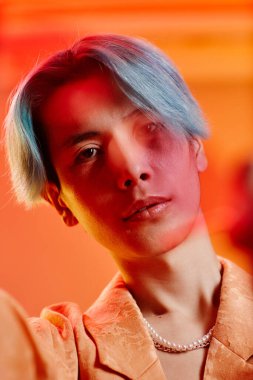 Renkli arka planda mavi saçlı Asyalı genç adamın dikey görüntüsü