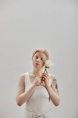 Beyaz gül tutan albinizmli güzel bir kızın dikey portresi, gözleri kapalı.