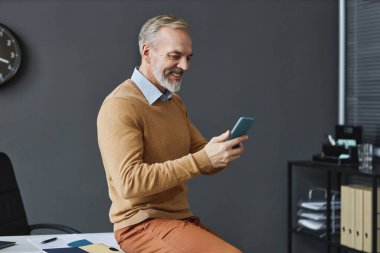 İş yerinde akıllı telefon kullanan ve gülümseyen, fotokopi çeken yakışıklı bir iş adamının yan görünümü.