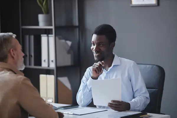 Portrait of smiling black man as HR recruiter listening to senior candidate at job interview