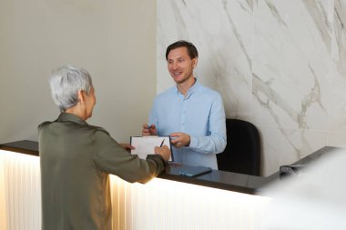 Gülümseyen genç bir adamın portresi yaşlı bir kadının klinikte doktor ziyaretine kaydolmasına yardım ediyor.