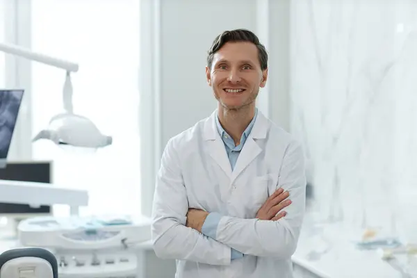 歯科診療所のカメラで笑顔の男性歯科医の肖像画をウエストし 腕を交差して立って スペースをコピー — ストック写真