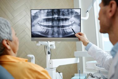 Klinikteki diş cerrahisi konsültasyonu sırasında ekrandaki diş röntgeni görüntüsünü gösteren erkek dişçinin arka plan görüntüsü
