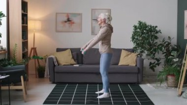 Spor giyimli, aktif, beyaz kadın sabah evde egzersiz yaparken dambıllarıyla çömelirken tam bir bıçak darbesi.