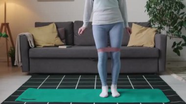 Beyaz yaşlı bir kadının evcil sabah fitness antrenmanı sırasında diz boyu çömelme hareketleri çekimleri.