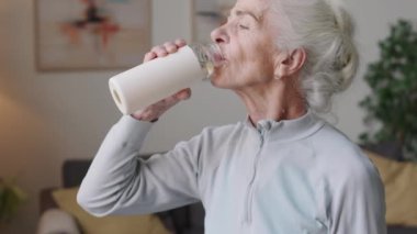 Beyaz yaşlı bir kadının spor salonundan sonra spor şişesinden su içtiği orta boy bir fotoğraf.