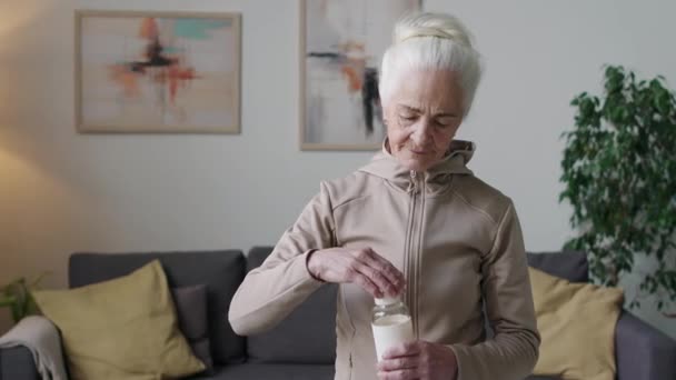 现代公寓里 身穿拉链帽摆的白种人老年妇女手持运动瓶在镜头前摆姿势的中影 — 图库视频影像