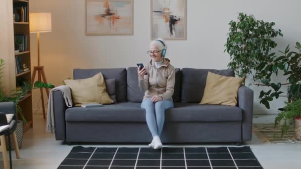 Apuñalada Completa Alegre Mujer Anciana Caucásica Auriculares Inalámbricos Sentados Sofá — Vídeos de Stock