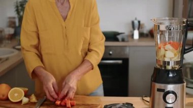 Modern mutfakta kahvaltı için vitamin içeceği hazırlarken portakallara havuç ve elmaya rulo havuç ekleyen orta boy beyaz yaşlı kadın fotoğrafı.